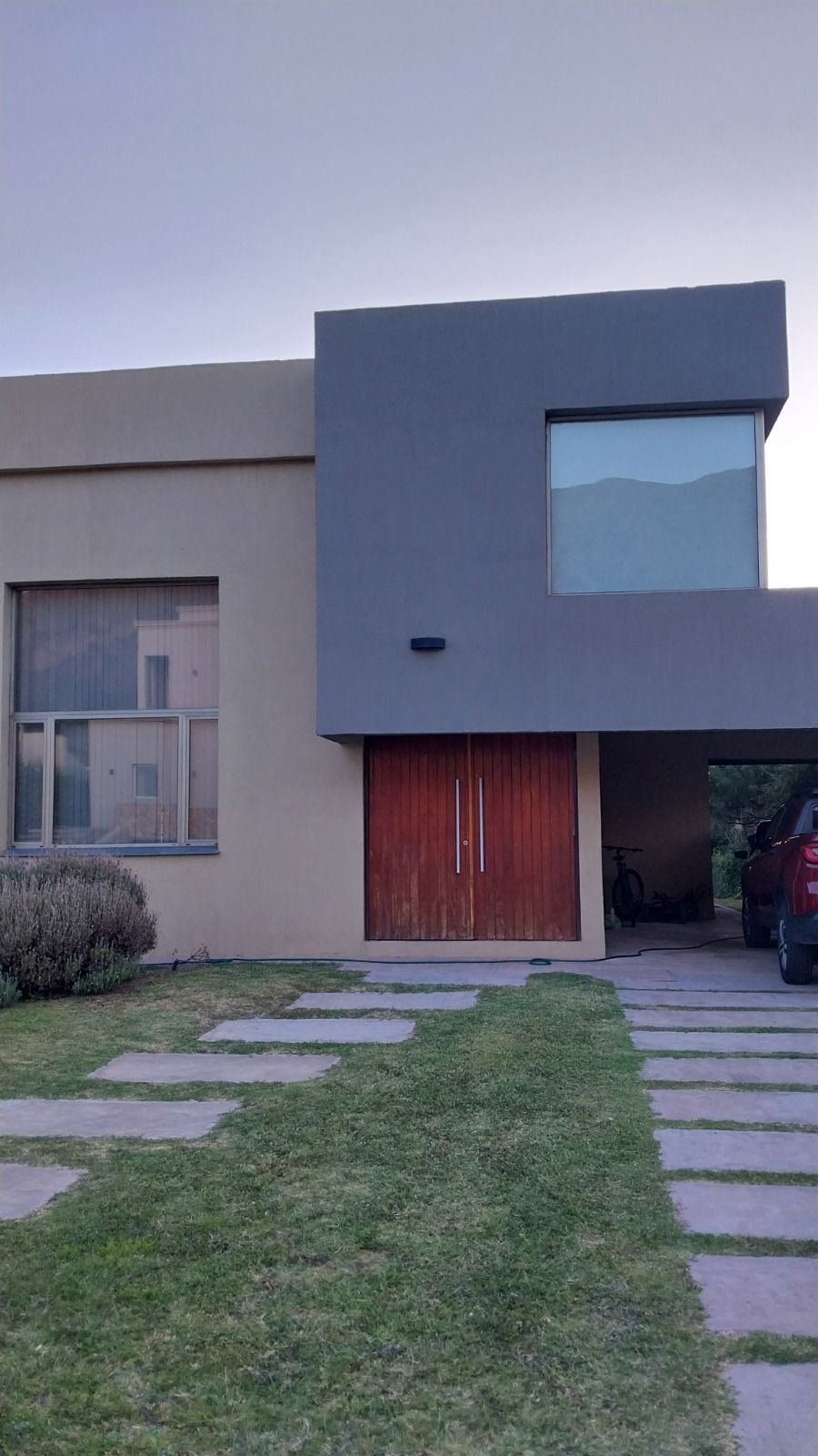 Fachada de dos plantas con puerta de acceso roja y sendero de lajas sobre el césped